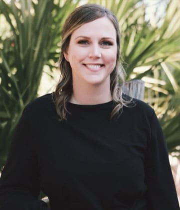 Woman in black shirt smiling at camera with green foliage background