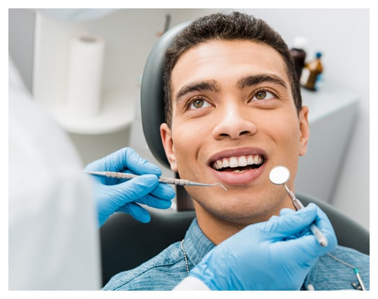 Man receiving dental examination in dentist's office with tools and mirror.