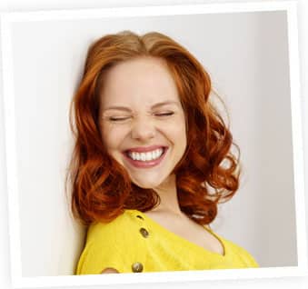Woman with red wavy hair smiling in yellow shirt against white background