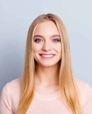 Smiling young woman with long blonde hair wearing a light pink top.