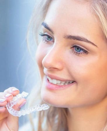 Young woman smiling while holding an invisible aligner tray for orthodontic treatment.