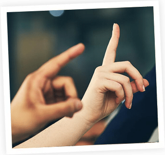 Two hands forming a heart shape gesture against a dark blurred background.