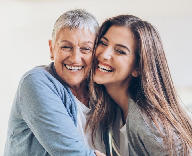 Senior woman and young woman smiling together against white background, embracing warmly.