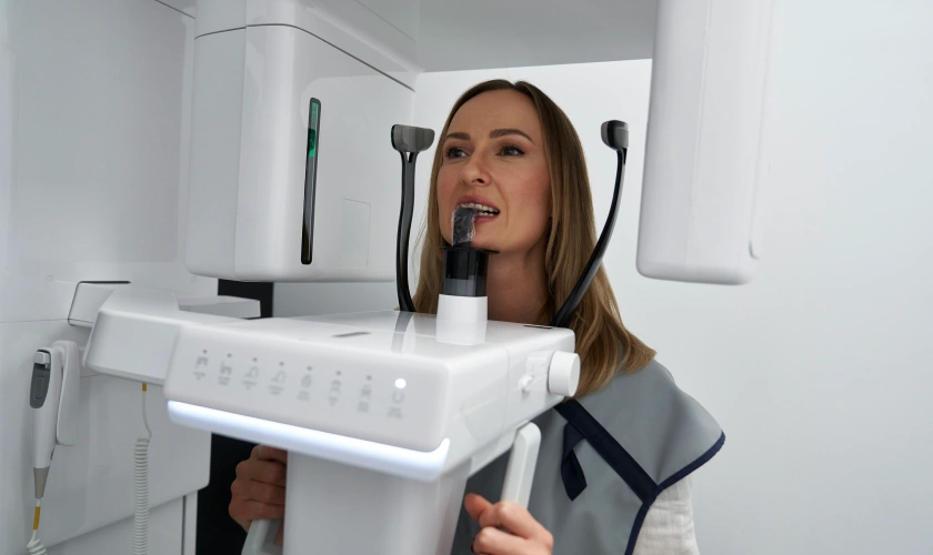 Woman demonstrating dental imaging equipment in modern clinical setting with white technology devices.