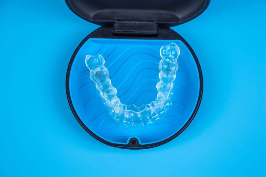 Clear orthodontic retainer displayed in open case against blue background.