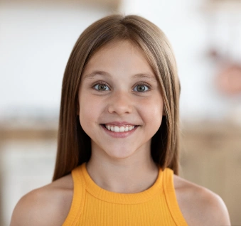 Smiling young girl wearing yellow tank top in bright indoor setting