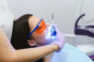 Patient receiving professional teeth whitening treatment with blue LED light in dental office.